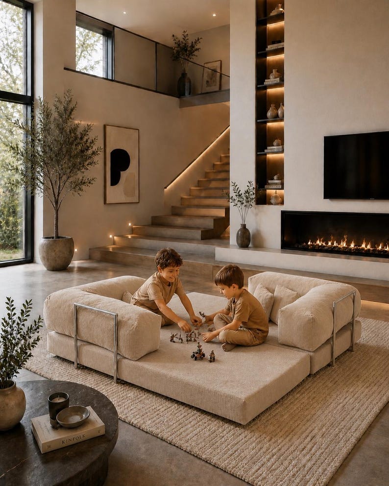 Puede incluir: Un sal&oacute;n moderno con un sof&aacute; modular beige, dos ni&ntilde;os jugando y una paleta de colores neutros. La habitaci&oacute;n cuenta con una chimenea, una ventana grande y una escalera que conduce a un segundo nivel. Una mesa de centro redonda con un libro y velas est&aacute; en primer plano.