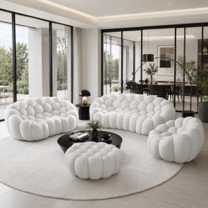 May include: A contemporary living room arrangement with a white, bubble-textured sofa, two armchairs, and an ottoman. A black coffee table with decor sits on a circular, light-coloured rug. Large windows offer a view of the garden.