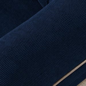 May include: Close-up of a section of a navy blue corduroy sofa. The fabric has a ribbed texture, with visible vertical lines. A silver-colored metal frame is visible on the edge of the sofa.