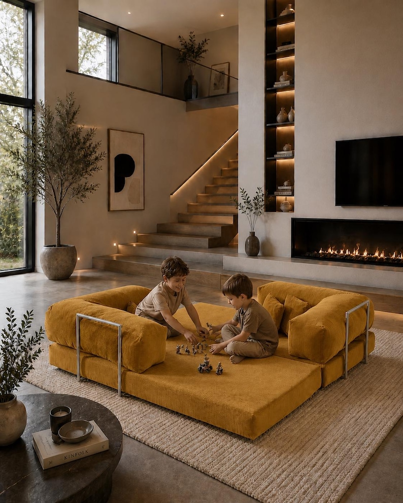 Puede incluir: Dos ni&ntilde;os jugando en un sof&aacute; modular amarillo mostaza con marcos de metal plateado. El sof&aacute; est&aacute; sobre una alfombra beige en una sala de estar moderna con chimenea, estanter&iacute;as empotradas y una escalera.
