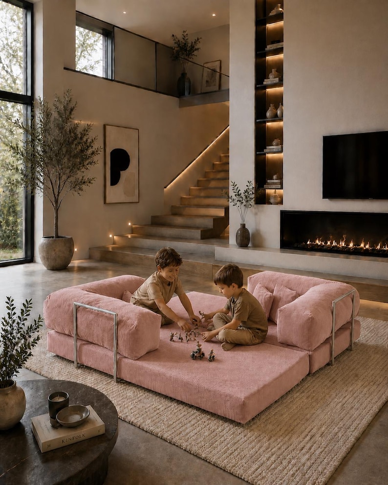 Puede incluir: Sal&oacute;n moderno con un gran sof&aacute; modular rosa. Dos ni&ntilde;os juegan en el sof&aacute;. La habitaci&oacute;n cuenta con chimenea, una ventana grande y una escalera. La decoraci&oacute;n es minimalista y neutra, con enfoque en la luz natural.