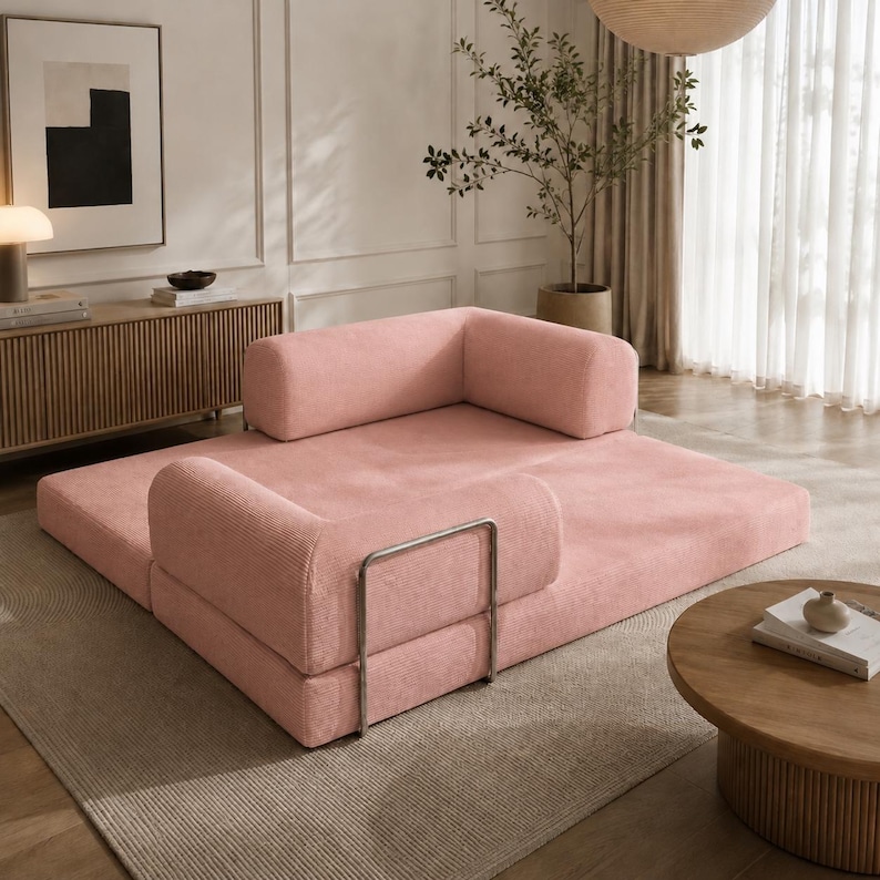 Puede incluir: Un sof&aacute; modular de pana rosa con reposabrazos redondeados y un coj&iacute;n cil&iacute;ndrico. El sof&aacute; tiene una estructura met&aacute;lica y est&aacute; sobre una alfombra de color neutro. El dise&ntilde;o es moderno y minimalista.