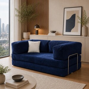 Puede incluir: Un sal&oacute;n moderno con un sof&aacute; de pana azul marino y un coj&iacute;n blanco. Una mesa de centro redonda y clara descansa sobre una alfombra beige. La habitaci&oacute;n incluye una ventana grande, obras de arte y plantas decorativas.