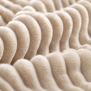 Puede incluir: Primer plano de una manta beige suave con un dise&ntilde;o acanalado texturizado. La tela de felpa tiene un patr&oacute;n ondulado, creando una sensaci&oacute;n de profundidad y comodidad. El color neutro sugiere un textil para el hogar acogedor.