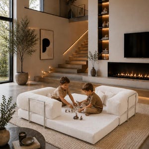 Puede incluir: Dos ni&ntilde;os jugando en un sof&aacute; modular blanco con soportes de metal plateado. El sof&aacute; est&aacute; sobre una alfombra beige en una sala de estar moderna con chimenea, estanter&iacute;as empotradas y una escalera. La habitaci&oacute;n tiene tonos neutros y luz natural.