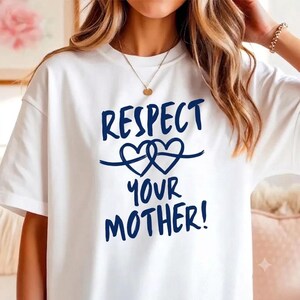 Può includere: Una t-shirt bianca a maniche corte con la scritta blu scuro "RESPECT YOUR MOTHER!" e un grafico di due cuori intrecciati tra le parole. Il capo presenta un girocollo e un design semplice e pulito sulla parte anteriore.