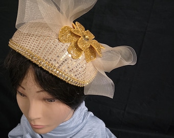 ラインストーンの花とリボンがあしらわれた、ゴールドのスパンコール付きファシネーターハット。
