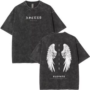 May include: Charcoal grey t-shirt with a worn effect. The front has the word "ASCEND" above "ATHLETIC" in white. The back shows white angel wings and the word "ELEVATE".