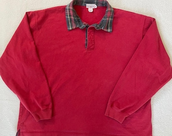 Puede incluir: Una camisa roja de manga larga con cuello. El cuello presenta un estampado de cuadros en tonos verdes, grises y rojos. La camisa tiene una tapeta abotonada en el escote y un corte relajado. La camisa está hecha de un material suave y cómodo.