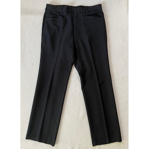 Puede incluir: Un pantalón negro. El pantalón tiene un diseño clásico de pierna recta con cierre de botón y cremallera. El pantalón tiene bolsillos delanteros y trabillas para el cinturón. La tela parece ser un material liso y sólido.