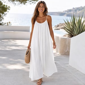 May include: A floor-length white maxi dress with thin spaghetti straps, a scoop neckline, and a loose, flowing silhouette. The dress is paired with a woven straw handbag and brown strappy sandals, creating a simple and clean aesthetic.