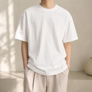 Op de afbeelding: Een effen wit T-shirt met korte mouwen en een ronde hals, gecombineerd met een lichtbeige broek. Het T-shirt heeft een relaxte pasvorm en een gladde, effen stof, wat zorgt voor een strakke en eenvoudige uitstraling voor dagelijks gebruik.