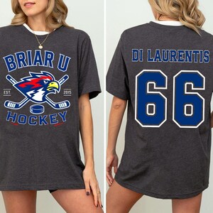 Puede incluir: Camiseta de hockey gris oscuro con cuello blanco. La parte delantera presenta un logotipo azul y blanco con un &aacute;guila roja, palos de hockey cruzados y las palabras "Briar U Hockey". La parte trasera muestra "Di Laurentis" y el n&uacute;mero "66" en azul.