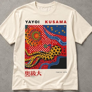 Puede incluir: Una camiseta de manga corta color crema con un estampado gráfico de Yayoi Kusama. El diseño incluye un fondo rojo con lunares blancos, una forma similar a un pulpo amarillo con puntos negros, formas azules y el texto YAYOI KUSAMA TOKYO 1998.
