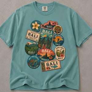Könnte beinhalten: Ein salbeigrünes Kurzarm-T-Shirt mit einer Collage aus Bali-Motivaufklebern. Die Grafiken zeigen eine Frangipani-Blüte, einen Tempel, eine Barong-Maske, einen Surfer, Reisterrassen, eine Meeresschildkröte, eine Kokosnuss und den Schriftzug BALI.