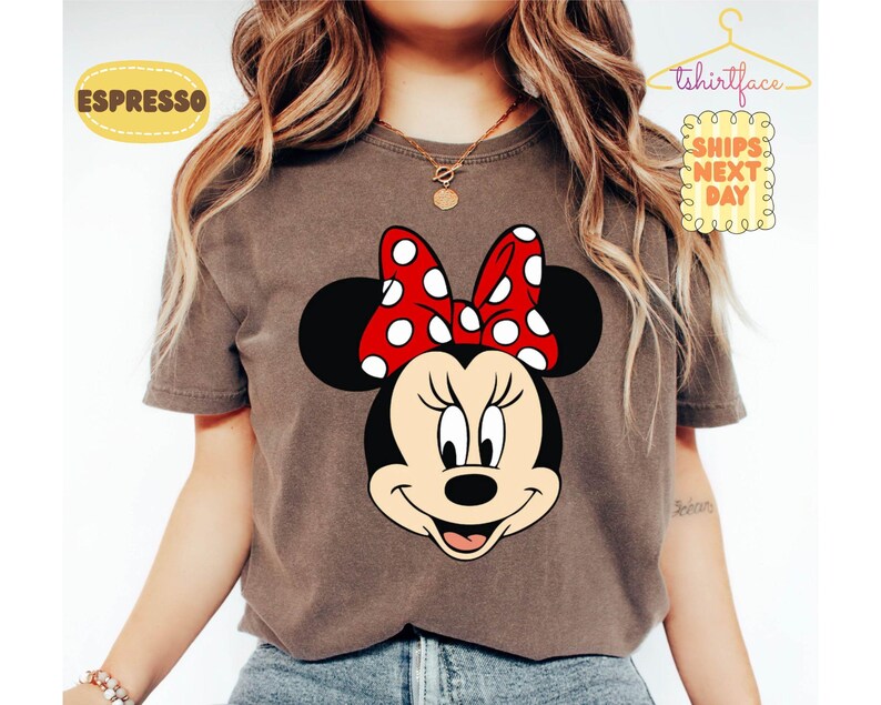May include: Espresso-colored t-shirt featuring a large graphic of Minnie Mouse's face. Minnie has a red bow with white polka dots. The shirt has the text "tshirtface" and "SHIPS NEXT DAY" on it.