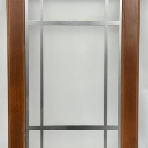 May include: A wooden cabinet door with a rectangular frame and a silver metal grid design. The wood has a warm brown tone, and the grid divides the glass into rectangular sections.