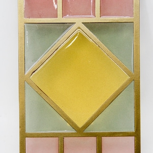 May include: A gold-framed decorative tile with a geometric design. The tile features a large yellow diamond shape in the center, surrounded by four smaller squares. The squares are in shades of pink and green.