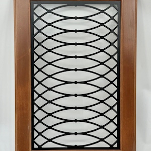 May include: A rectangular wooden cabinet door with a black metal decorative insert. The insert features an intricate, repeating pattern of interconnected ovals. The wood frame is a warm brown color, and the metal insert is black.