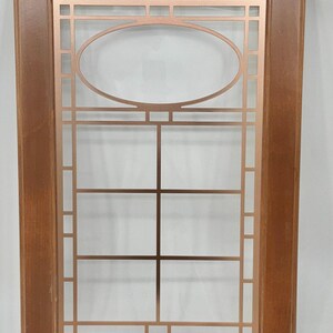 May include: A rectangular cabinet door frame made of medium-toned brown wood. The centre panel features a metallic copper-coloured grid insert with a prominent horizontal oval shape at the top, creating a geometric pattern within the wooden frame.