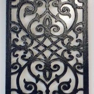 May include: Black wrought iron decorative panel with an ornate, symmetrical design. The panel features scrolling vines, floral elements, and a central diamond pattern. The rectangular panel is suitable for wall decor.