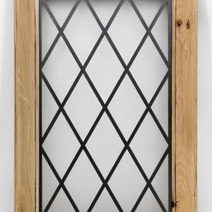 Può includere: Un telaio di finestra in legno con un motivo a rombi neri. La cornice è in legno di colore chiaro e il motivo a rombi è in metallo nero. Il vetro della finestra è un elemento decorativo.