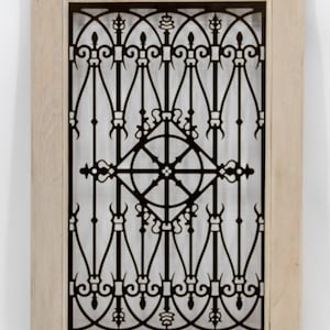 May include: A decorative black metal grillwork panel with an ornate design, set within a light-colored wooden frame. The intricate pattern features symmetrical curves and geometric shapes, suitable for home decor.