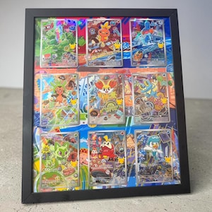 May include: A black rectangular frame containing nine collectible trading cards arranged in a three-by-three grid. Each card features a colorful cartoon creature illustration with holographic details and a small gold Pikachu icon in the corner.