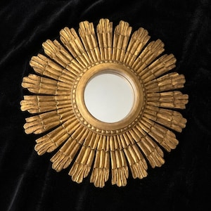 May include: A circular wall mirror featuring a gold-toned frame with a sunburst design. The frame consists of numerous radiating, petal-like segments surrounding a central, smooth, reflective glass mirror surface with a beaded inner border.