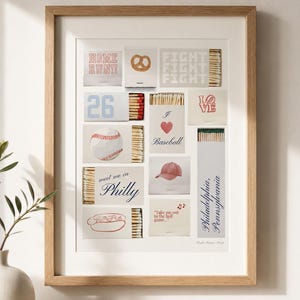 Op de afbeelding: Ingelijste kunst met honkbalthema-illustraties en tekst. Het kunstwerk bevat afbeeldingen van een honkbal, een pretzel, een hotdog en een honkbalpet. Tekst bevat "HOME RUN!!", "FIGHT FIGHT FIGHT", "26", "I LOVE", "meet me in Philly" en "Take me out to the ball game".
