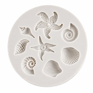 May include: A circular white silicone mould featuring seven distinct recessed cavities shaped like various sea life, including a starfish, a spiral shell, a conch shell, a textured shell, and a fan-shaped shell, all arranged on a flat surface.