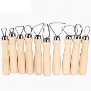 May include: A collection of nine pottery sculpting tools. Each tool features a light-coloured wooden handle and a stainless steel head in various shapes, such as loops and triangles. The tools are displayed in a row against a white backdrop.