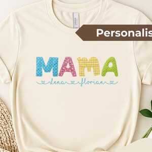Könnte beinhalten: Cremefarbenes T-Shirt mit dem Wort "MAMA" in bunten, gemusterten Buchstaben. Darunter stehen die Namen "Lena" und "Florian" in Schreibschrift. Das Shirt hat ein "Natural"-Label und ein "Personalisiert"-Label.