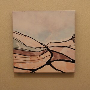 May include: A square canvas wall art piece featuring an abstract landscape design. The artwork displays soft, muted tones of peach, beige, and pale blue, overlaid with bold, dark black lines that create a sense of depth and movement across the surface.