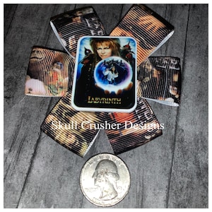 May include: A white bow with a black and brown ribbon featuring a Labyrinth movie poster with the text "Labyrinth" and a picture of David Bowie as Jareth the Goblin King. The bow is on a wooden surface.