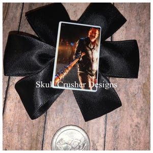 May include: A black bow with a square image of a man holding a baseball bat. The image is on a white background and has the text "Skull Crusher Designs".