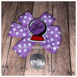 May include: Purple and white polka dot bow with a 8-bit style 8-ball with the text "SHIT HAPPENS" on it. Skull Crusher Designs is written on the bow.