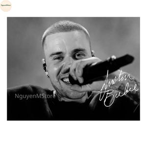 Peut inclure: Photographie en noir et blanc d'une personne souriante tenant un microphone. L'image comprend la signature "Justin Bieber". La personne a les cheveux courts et porte un haut sombre.
