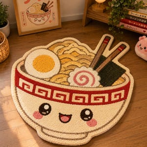 May include: A beige, bowl-shaped rug with a smiling ramen face design. The rug features a red and white border, with a yellow egg, noodles, and chopsticks. The rug is on a wooden floor, with a framed picture of ramen in the background.