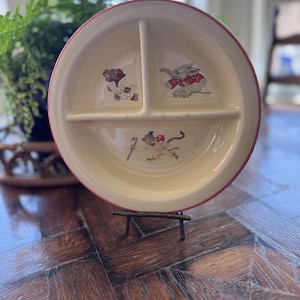 May include: A vintage divided plate with a cream-colored surface and a pink rim. The plate features three sections, each with a cartoon animal illustration. The animals include a dog, an elephant, and a mouse.