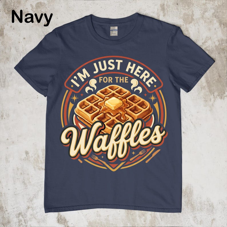 Puede incluir: Camiseta azul marino con un gr&aacute;fico de gofres. El gr&aacute;fico presenta una pila de gofres con mantequilla y el texto "I'M JUST HERE FOR THE Waffles". El dise&ntilde;o incluye colores naranja, amarillo y marr&oacute;n.