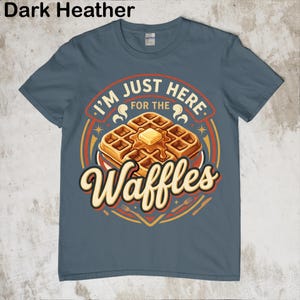 Puede incluir: Camiseta azul oscuro jaspeado con un gr&aacute;fico de gofres. El gr&aacute;fico dice "I'm just here for the Waffles" en un dise&ntilde;o circular con una ilustraci&oacute;n de gofre y mantequilla. La camiseta es de cuello redondo y manga corta.