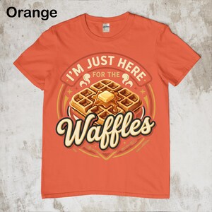 Puede incluir: Camiseta naranja con un gr&aacute;fico de gofres. El gr&aacute;fico presenta una pila de gofres con mantequilla y el texto "I'M JUST HERE FOR THE Waffles". La camiseta es de color naranja liso.