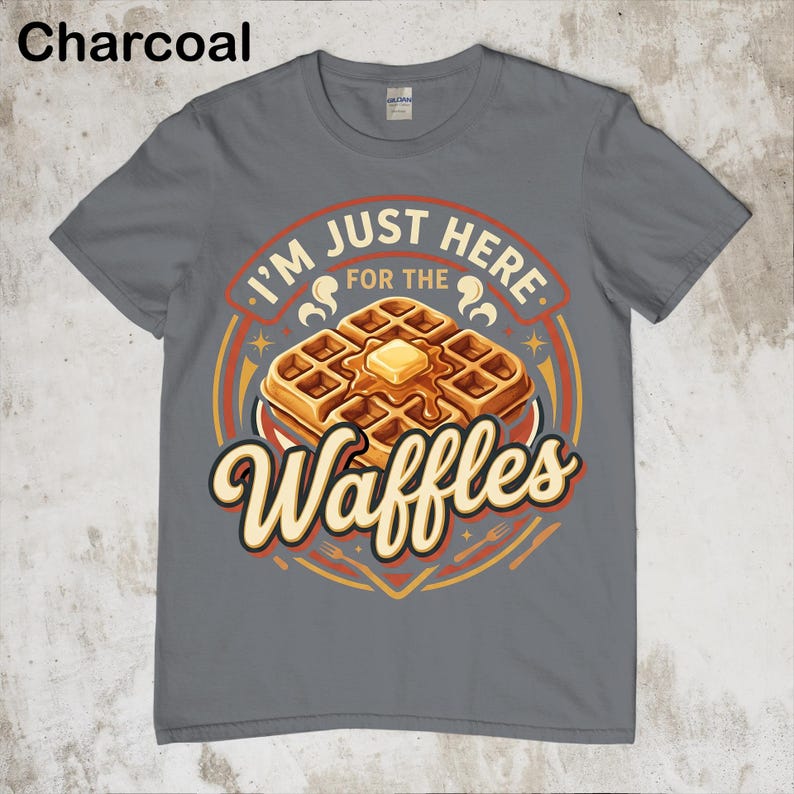 Puede incluir: Camiseta gris carb&oacute;n con un gr&aacute;fico de gofres. El gr&aacute;fico presenta una pila de gofres con mantequilla y el texto "I'm just here for the Waffles". El dise&ntilde;o es en tonos naranja, amarillo y marr&oacute;n.