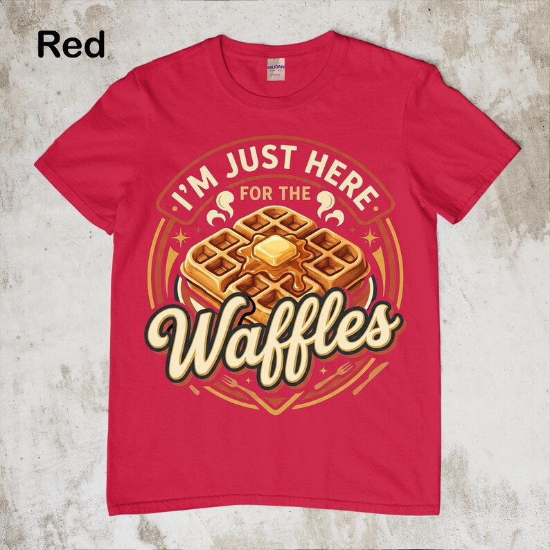 Puede incluir: Camiseta roja con un gr&aacute;fico de gofres. El gr&aacute;fico presenta una pila de gofres con mantequilla y el texto "I'M JUST HERE FOR THE Waffles". El dise&ntilde;o incluye un borde circular con estrellas e ilustraciones de tenedores y cuchillos.