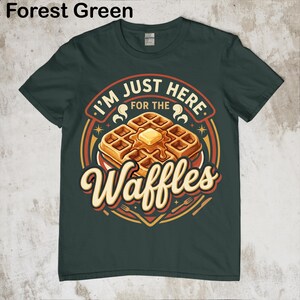 Puede incluir: Camiseta verde bosque con un dise&ntilde;o de gofres. El texto en el gr&aacute;fico dice "I'M JUST HERE FOR THE Waffles". Los gofres son dorados con mantequilla. Una camiseta divertida con tem&aacute;tica de comida.