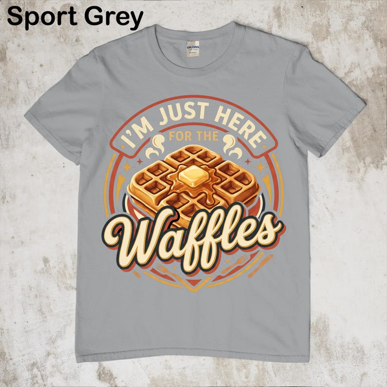 Puede incluir: Camiseta gris deportivo con un gr&aacute;fico de gofres. El gr&aacute;fico presenta una pila de gofres con mantequilla y el texto "I'm just here for the Waffles". El dise&ntilde;o es en tonos marrones, naranjas y amarillos.