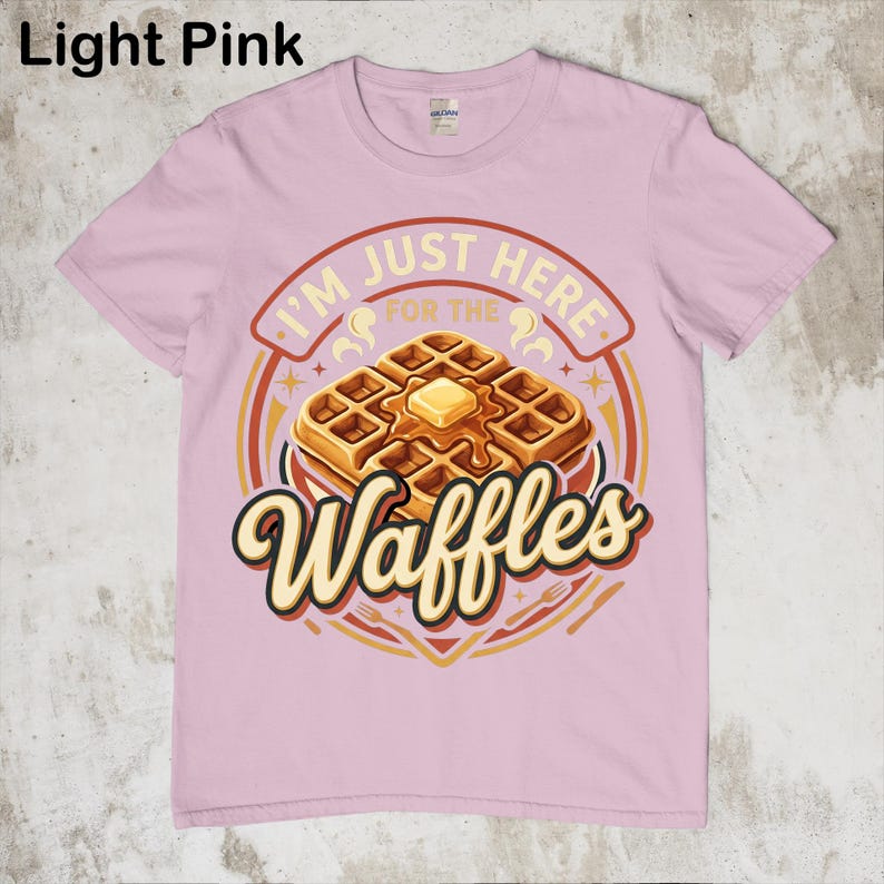 Puede incluir: Camiseta rosa claro con un dise&ntilde;o de gofre. El dise&ntilde;o dice "I'M JUST HERE FOR THE Waffles" en un c&iacute;rculo con un gofre con mantequilla. La camiseta es de cuello redondo.