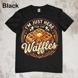 Puede incluir: Camiseta negra con un gr&aacute;fico de gofres. El dise&ntilde;o presenta una pila de gofres con mantequilla y el texto "I'm just here for the Waffles". El dise&ntilde;o es en tonos marrones, amarillos y rojos.