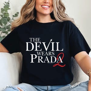May include: Black t-shirt with the text "THE DEVIL WEARS PRADA 2" in white and red. The shirt features a classic movie title design. The text is centered on the front of the shirt.